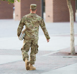 US soldier in uniform walking towards a building with books under his arm