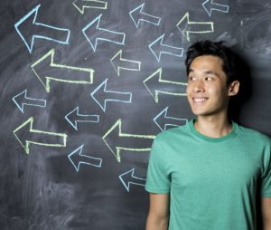 Man standing in front of a dark chalkboard with arrow signs drawn pointing.