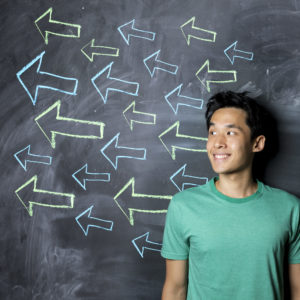 Man standing in front of a dark chalkboard with arrow signs drawn pointing.