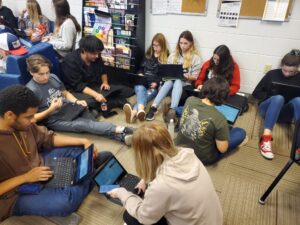 Students sitting around on the floor. Applying for colleges on their electronic devices