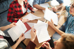 A group of people comparing notes on a table of messy papers.