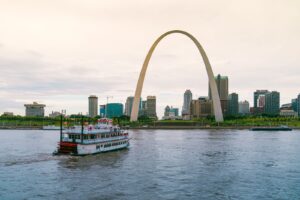 The Gateway Arch with St. Louis in the background as a river boat cruises along the river.