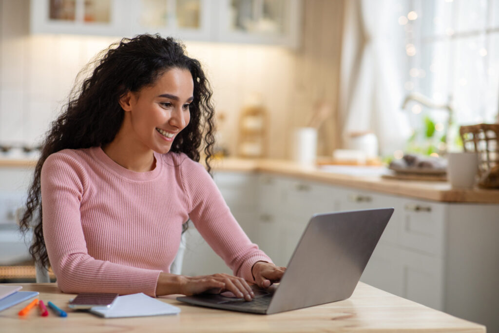 A woman working on her laptop in the kitchen of her house.