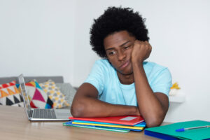 Student looking board and leaning against their hand as their other arm rests against their unopened notebooks.