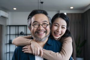 A middle-aged asian couple hugging, smiling, and laughing.
