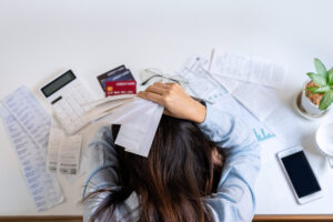 a student leaning over in frustration on top of all the bills and financial information she is dealing with.