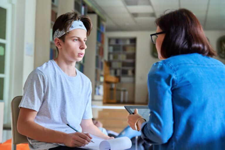 a school psychologist talking to a young student. He is taking notes while looking at her.