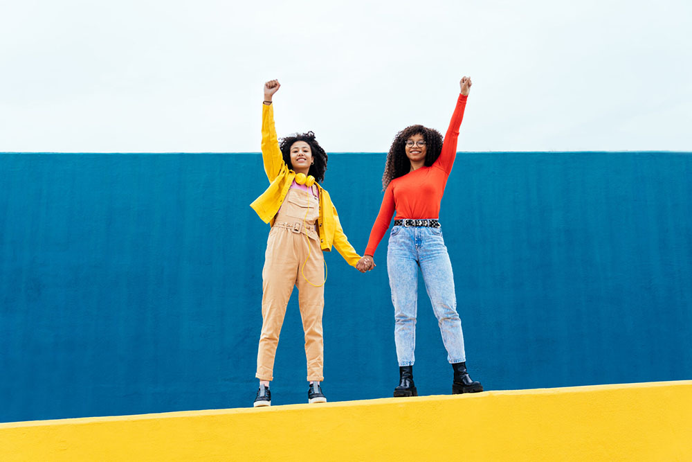 Two young women posing with their fists raising up to the sky and holding hands.