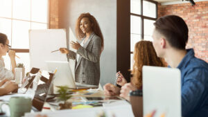 A black woman leading a business meeting and pointing at an easel of paper.