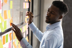 A black man mapping out something on sticky notes on a window.