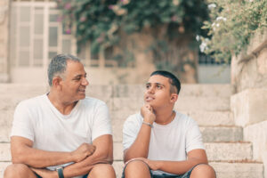 A teen boy and his father having a conversation on the stairs.