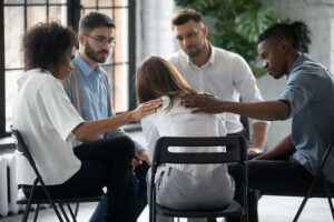 A supportive group console a woman who is facing away from the camera, she looks distraught.