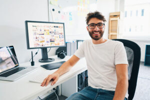 A bearded man smiling towards the camera showing off his computer with his portfolio on display.