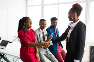 Three students meeting a local business woman. The woman in the front is shaking her hand. The two men behind her are just watching the business woman.