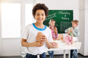 a young student smiling and holding a model of the human brain.