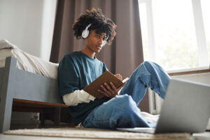 Low angle portrait of teenage African-American student sitting on floor in their room and studying
