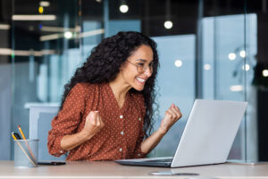 Hispanic woman celebrates her victory while sitting at her computer.