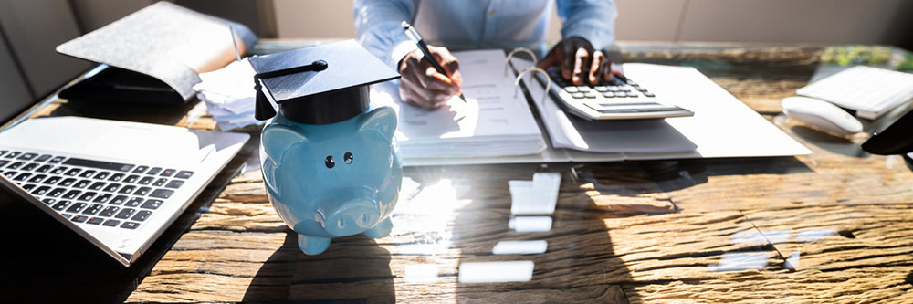 a piggy bank with a graduation hat as a student works on financial planning in the background.