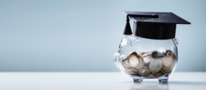 a piggy bank with a graduation hat as a student works on financial planning in the background.