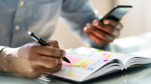 A black man writing down a schedule inside of his planner.